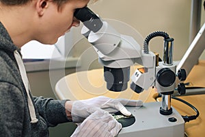 Young man repairing computer components in service center using microscope. Electronics repair and fix service concept.