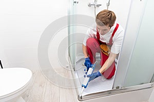 Young man repairing door of shower cabin in bathroom.