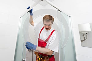 Young man repairing door of shower cabin in bathroom.