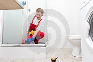 Young man repairing door of shower cabin in bathroom.