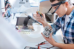 Young man repairing drones chip with a screwdriver