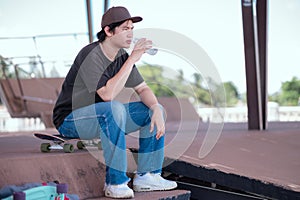Young man rested to drink water after exhausting his skateboarding
