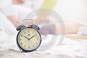 Young man resting on a beed reading a book. Alarm clock