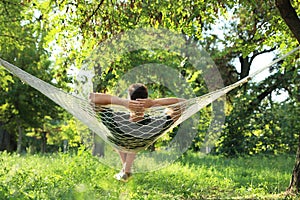 Young man resting in comfortable hammock at garden