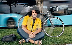 Young man resting after cycling on his bike in the city street. Male student with curly hair in yellow shirt with a bicycle