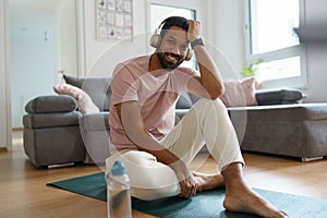 Young man resting after home workout and meditation, morning or evening workout routine, listening to music through