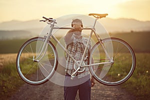Young man with retro bicycle in sunset on the road, fashion photography on retro style with bike