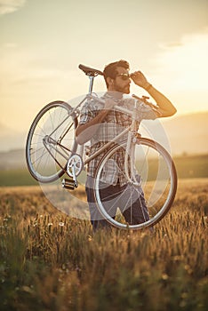 Mladý muž s retro bicyklom pri západe slnka na ceste, módna fotografia v retro štýle s bicyklom