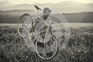 Mladý muž s retro bicyklom pri západe slnka na ceste, módna fotografia v retro štýle s bicyklom