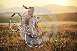 Mladý muž s retro bicyklom pri západe slnka na ceste, módna fotografia v retro štýle s bicyklom