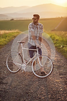 Mladý muž s retro bicyklom pri západe slnka na ceste, módna fotografia v retro štýle s bicyklom