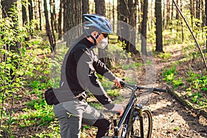 Young man ride mountain bike in forest. Young athletic man riding a bicycle in park. Male cyclist wearing face respirator, with