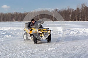 Young man rides ATV on ice on snow frozen lake in cold sunny winter day
