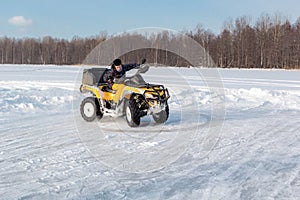 Young man rides ATV on ice on snow frozen lake in cold sunny winter day