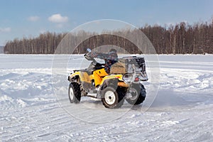 Young man rides ATV on ice on snow frozen lake in cold sunny winter day