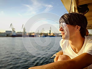 Young man rides on a tourist ship about Dnieper river on the background of the Kherson port on a sunny summer day. Profile