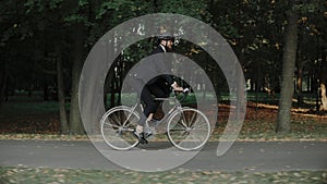 Young man riding a bike in city park wearing business suit and helmet, side view