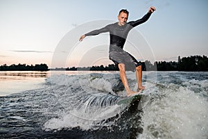 Young man riding down the river on a wake board at the evening