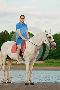 Young man riding a horse at sunset on the beach. Man with a horse in the rays of the sun by the sea.