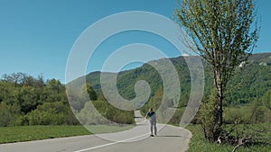 Young man riding on longboard on country road in summer day.