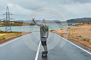 Young man riding a longboard on empty winding mountain road in summer, rear view.