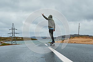 Young man riding a longboard on empty winding mountain road in summer, rear view.