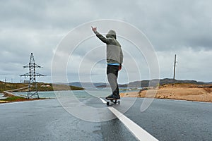 Young man riding a longboard on empty winding mountain road in summer, rear view.