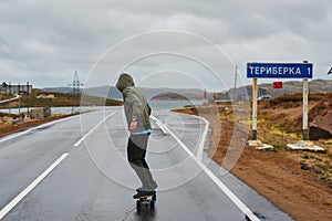 Young man riding a longboard on empty winding mountain road in summer, rear view.