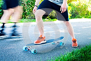 Young man riding on a longboard. Longboard on the road in sunny weather. People around skateboard.