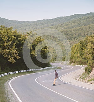 Young man riding on a longboard on the road.