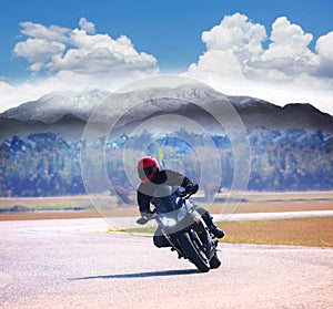 young man riding motorcycle on asphalt road against mountain highways background use for people activities on holiday vacation