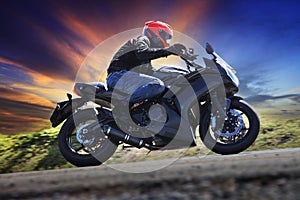 young man riding motorcycle on curve of asphalt country road against dusky sky use for sport activities,male leisure and journey