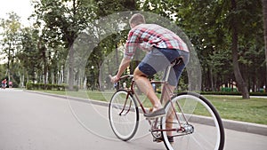 Young man riding vintage bicycle at the park alley. Sporty guy cycling outdoor. Healthy active lifestyle. Rear Back view