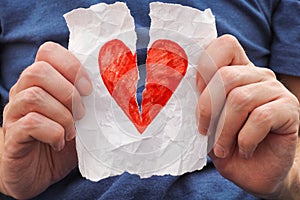 Young man ripping red heart on a piece of paper.