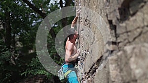 Young man rock climber with naked torso climbs on a granite cliff, gripping hold but falling