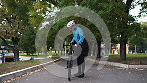 A young man rolls a bicycle in the park, sits on it and begins to ride