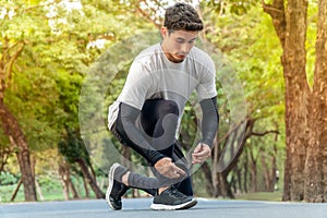 Young man runner tying shoelace in park ready for running in morning . sport outdoors healthy lifestyle in summer . prepare for