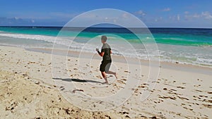 Young man running barefoot on beach, slow motion