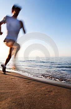 Young man running on a beach at sunrise. Motion blur effect.