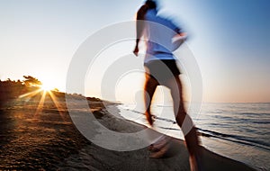 Young man running on a beach at sunrise. Motion blur effect.