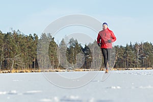 Young man running outdoors in winter snowy sunny forest