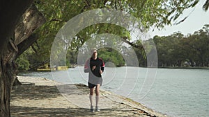 A young man running on a pathway beside lake towards camera