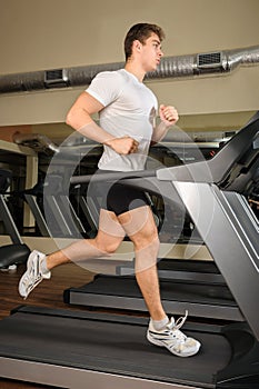 Young man running at treadmill in gym
