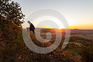 Young man running up to hill in Czech central mountain valley at sunrise. Outdoor landscape
