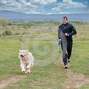 Young man running with your golden retriever dog on the meadow