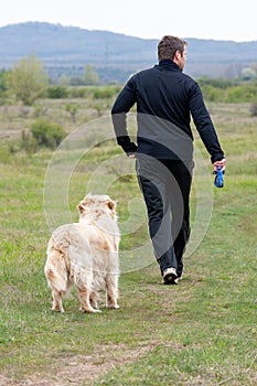 Young man running with your golden retriever dog on the meadow