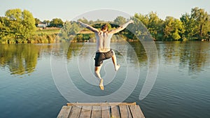 A young man runs along a wooden pier and jumps into the lake