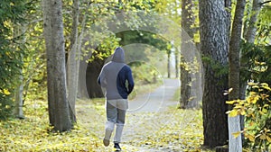 Young man runs in the autumn park. The runner is engaged in athletics. Sports lifestyle concept. Back view of the