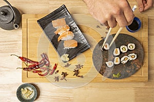 Young man's hand holding a maki roll from a plate next to other sushi dishes