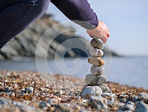 Young man`s hand lays a stone on a stone cairn on the beach